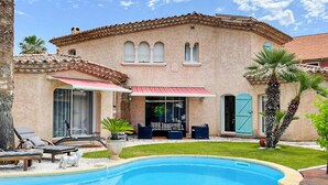 Une maison de style méditerranéen dotée d’une piscine, d’un espace salon extérieur et de palmiers.