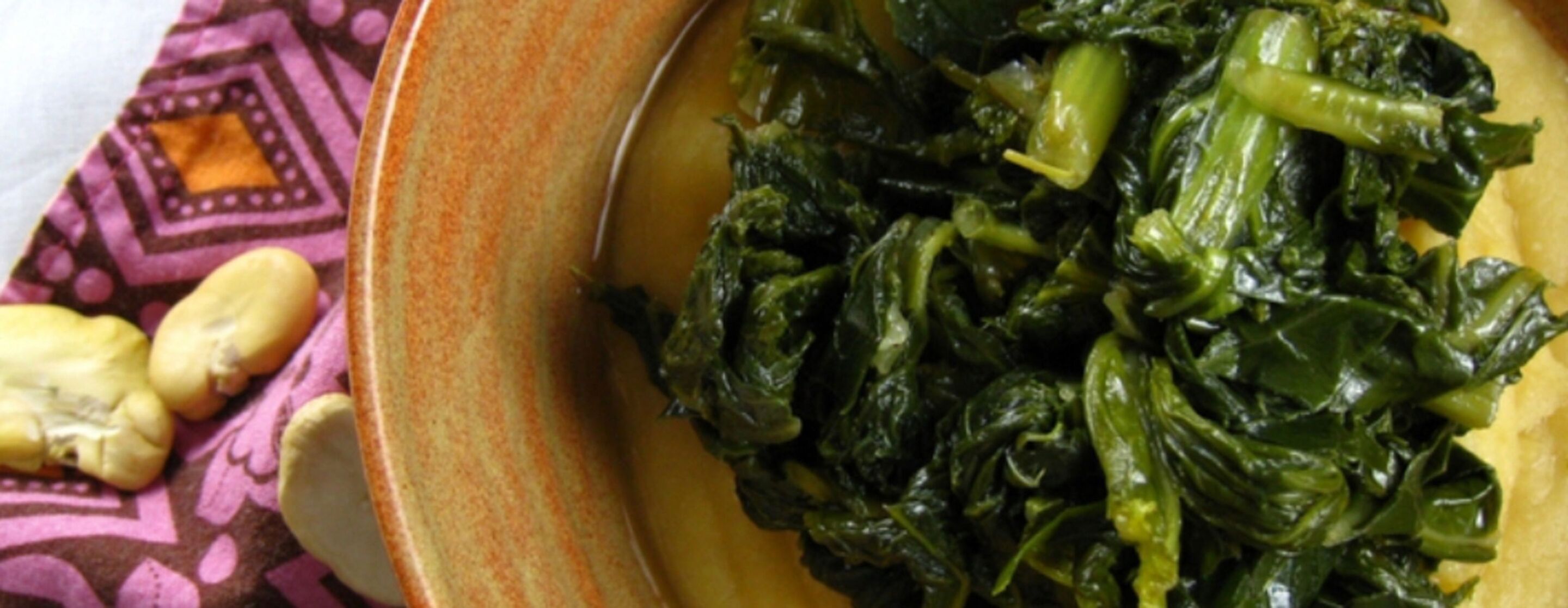 A plate of greens and a bowl of food, possibly a stew or curry, on a patterned tablecloth.