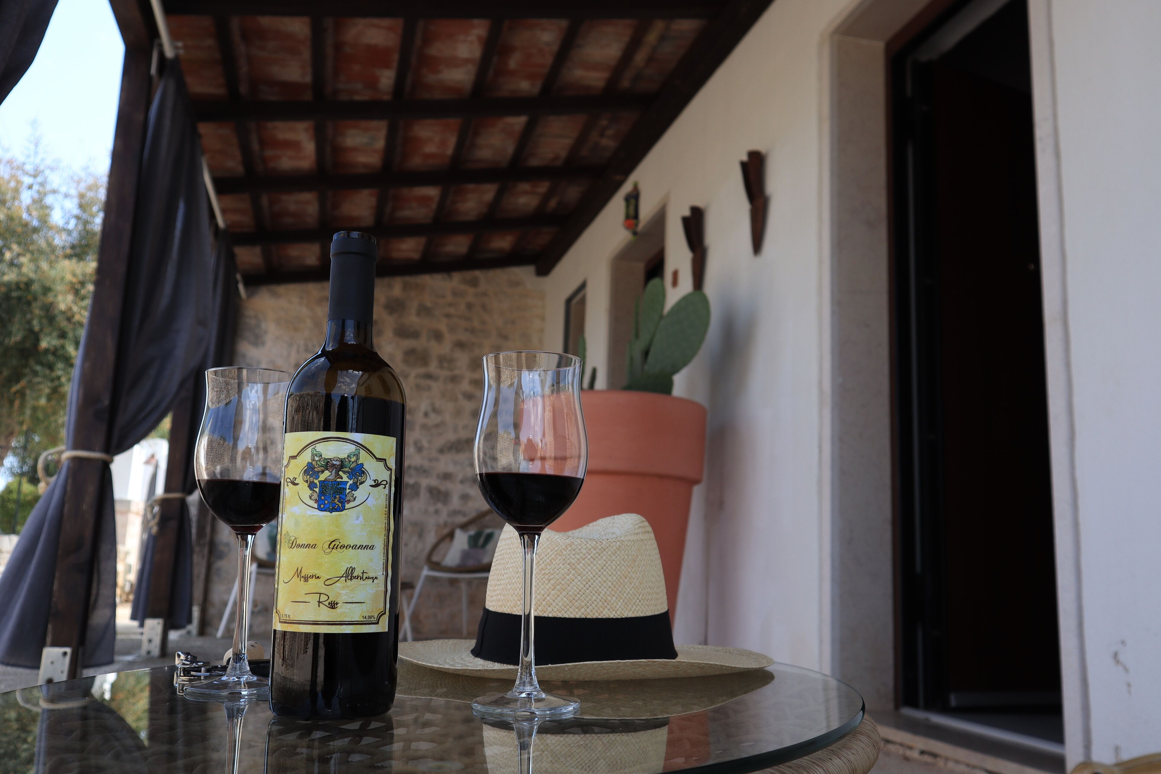 Una mesa con una botella de vino, dos copas de vino tinto y un sombrero de paja.