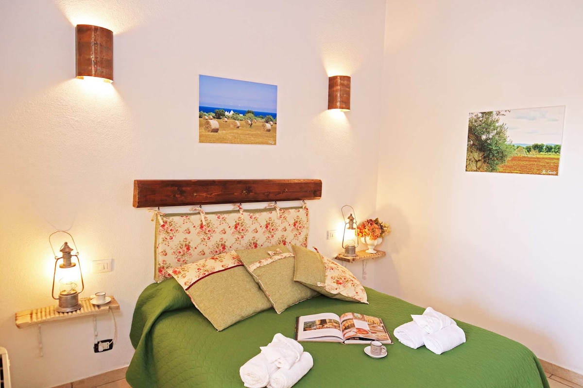 Ein ordentlich bezogenes Bett mit grüner Bettwäsche, einem Holz-Kopfteil und zwei an der Wand befestigten Lampen.