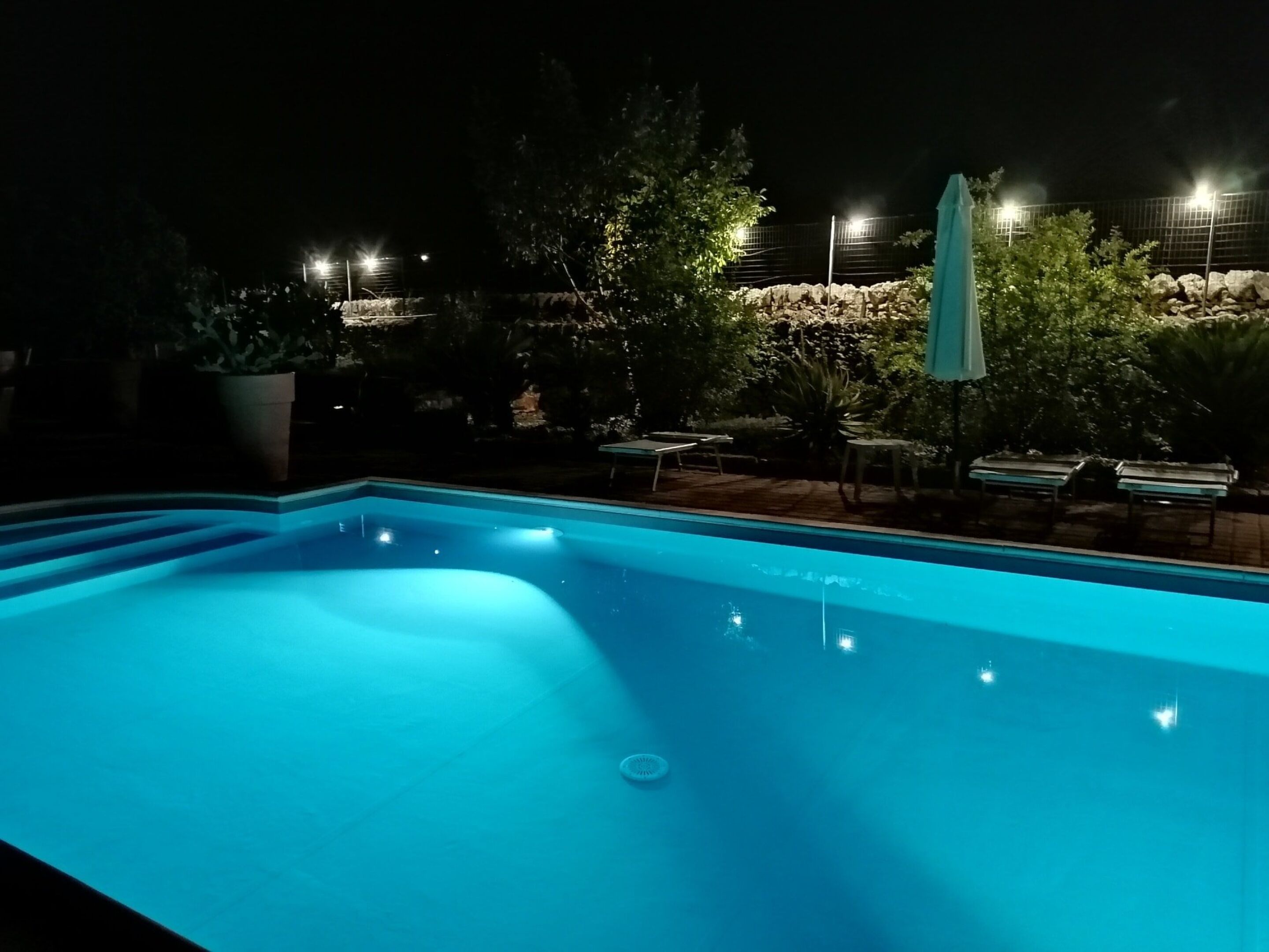 A swimming pool at night with surrounding trees and a stone wall.