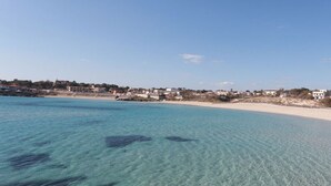 Vista costeira com águas turquesa cristalinas, praia arenosa e edifícios à beira-mar.