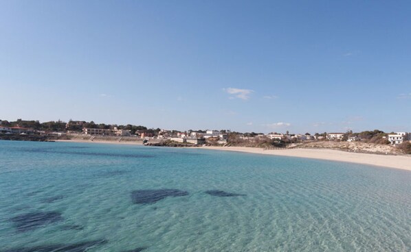 Une vue sur la côte, avec une eau turquoise et limpide, une plage de sable et des bâtiments qui bordent le rivage.