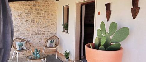 Un patio de paredes de piedra con dos sillas de mimbre, un cactus grande en maceta y decoración rústica.