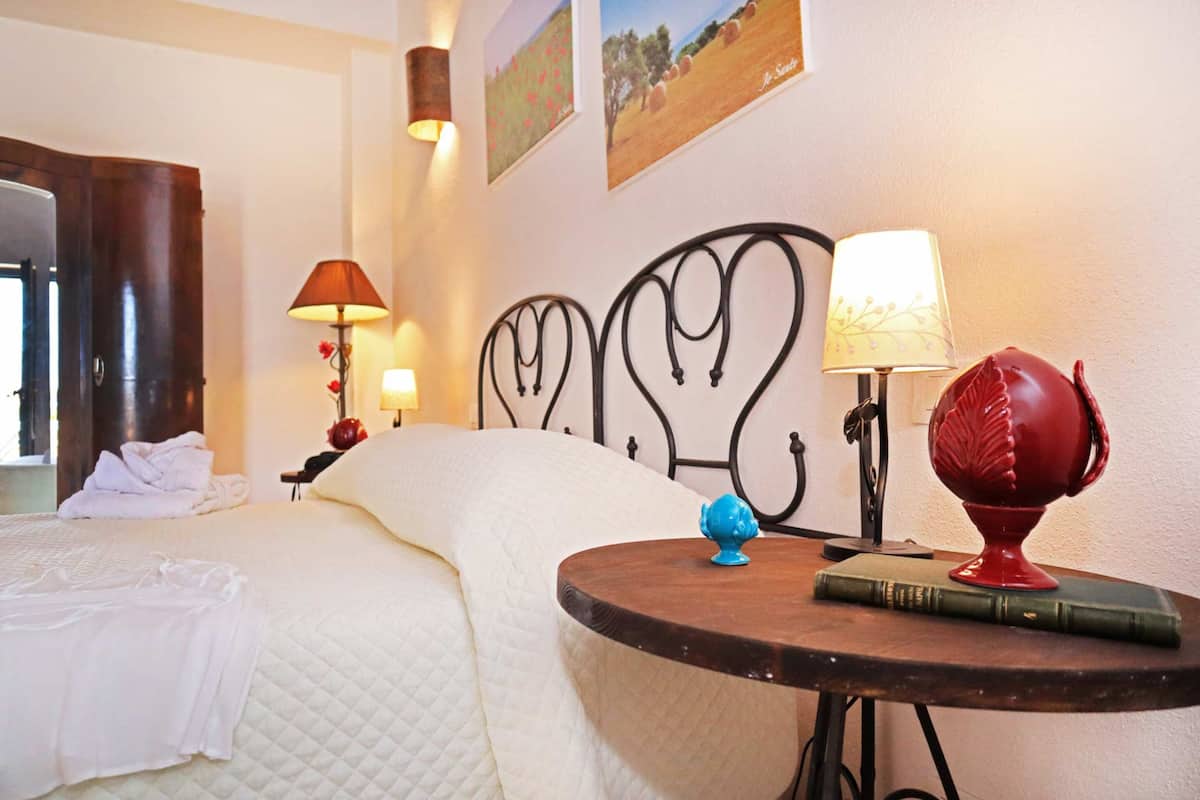 A hotel room with a bed, a round table with a lamp, a globe, and a book.