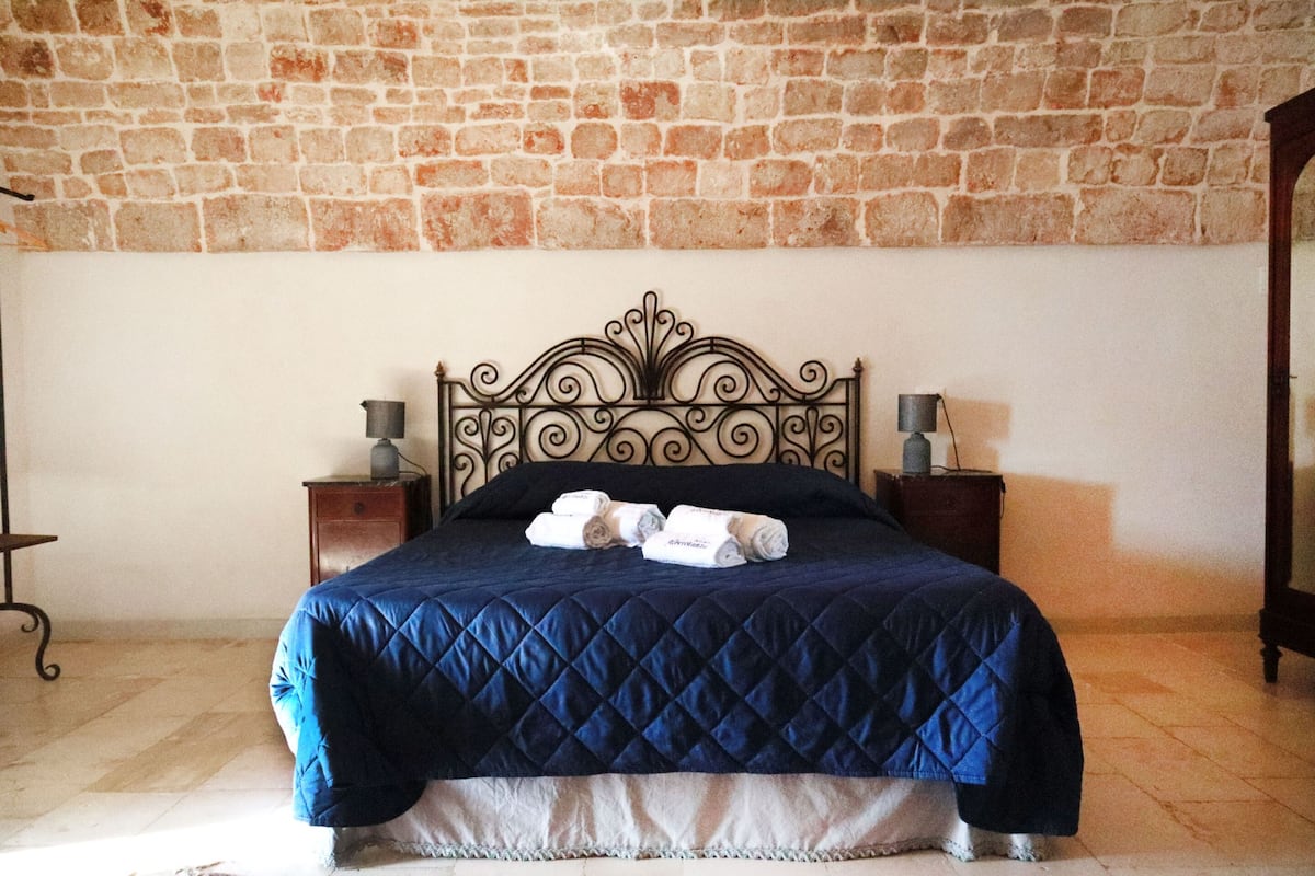A bed with a quilted blue cover, two bedside tables with lamps, and a brick wall.
