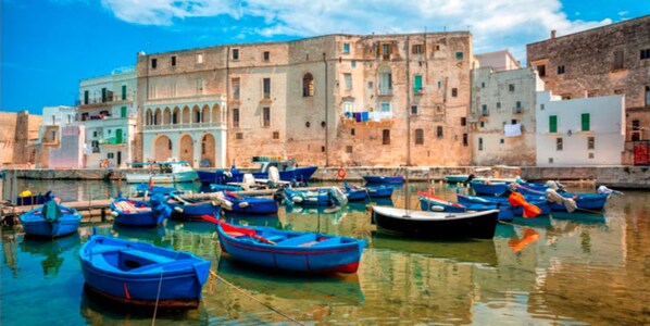 Un port où sont amarrés des bateaux, un bâtiment orné d’arches et un ciel dégagé.
