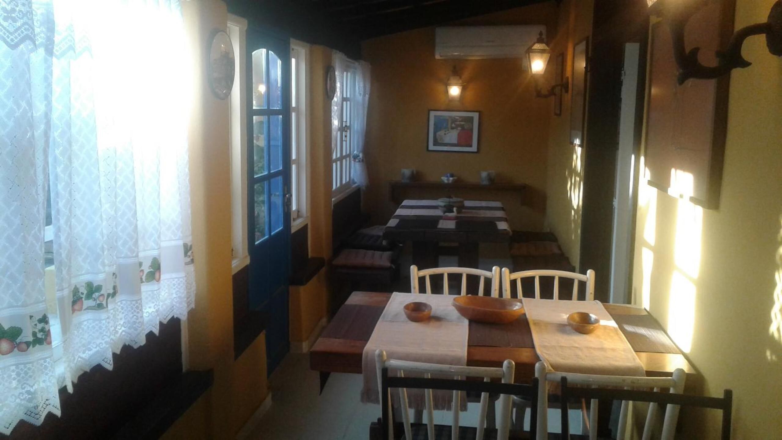 A narrow hallway with tables and chairs, a door, and a window with lace curtains.