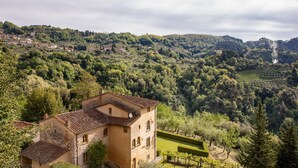 A rustic building with a tiled roof, surrounded by lush greenery and a hilly landscape. - Casa Gabriello (Pescaglia)