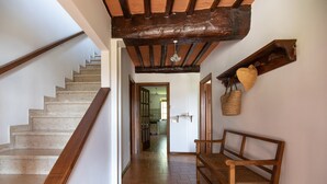 A staircase with wooden handrails, a bench, and a wall-mounted shelf with a heart-shaped object and a woven bag. - Casa Gabriello (Pescaglia)