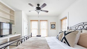 Une chambre à coucher avec un lit, un ventilateur de plafond, une télévision et une fenêtre avec des stores.