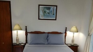 Un dormitorio con una cama grande, dos mesitas de noche con lámparas, un cabecero de madera, un cuadro enmarcado en la pared y una ventana con cortinas.