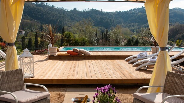 Eine Holzterrasse mit Liegestühlen und einem Pool mit Blick auf eine gebirgige Landschaft.