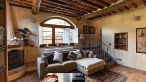 Ein gemütliches Wohnzimmer mit Holzbalkendecke, Kamin, einer Couch und einer Treppe.