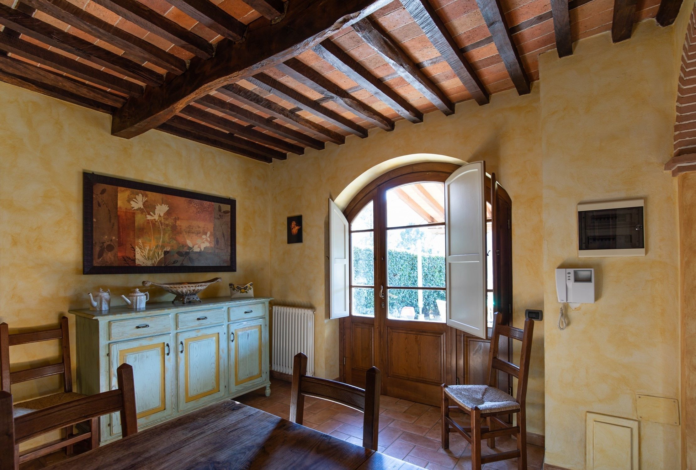 Ein Essbereich mit Holzböcken und Tisch, ein cremefarbenes Schränkchen mit Schubladen, ein Bild an der Wand und ein Fenster mit Blick auf Grünflächen.