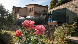 A rustic stone building with a tiled roof, a garden with pink roses, and a stone wall. - Casa Paola (Camaiore)
