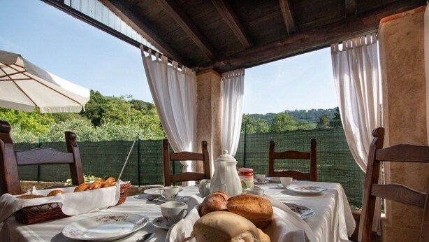 An outdoor dining area with a table set for breakfast, including bread, pastries, and tea. - Casa Paola (Camaiore)