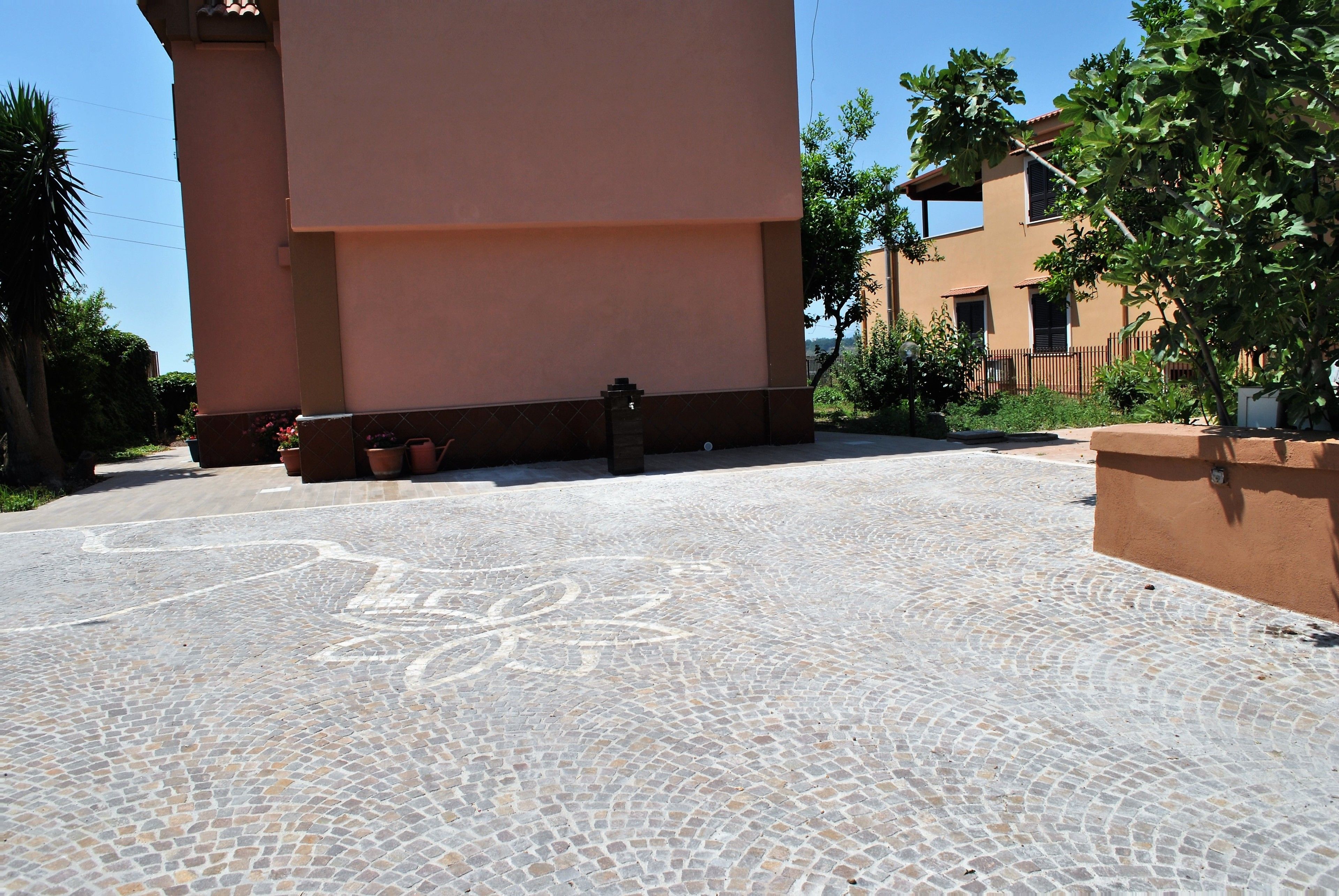 A courtyard with a tiled floor, a building with a pink facade, and a tree.