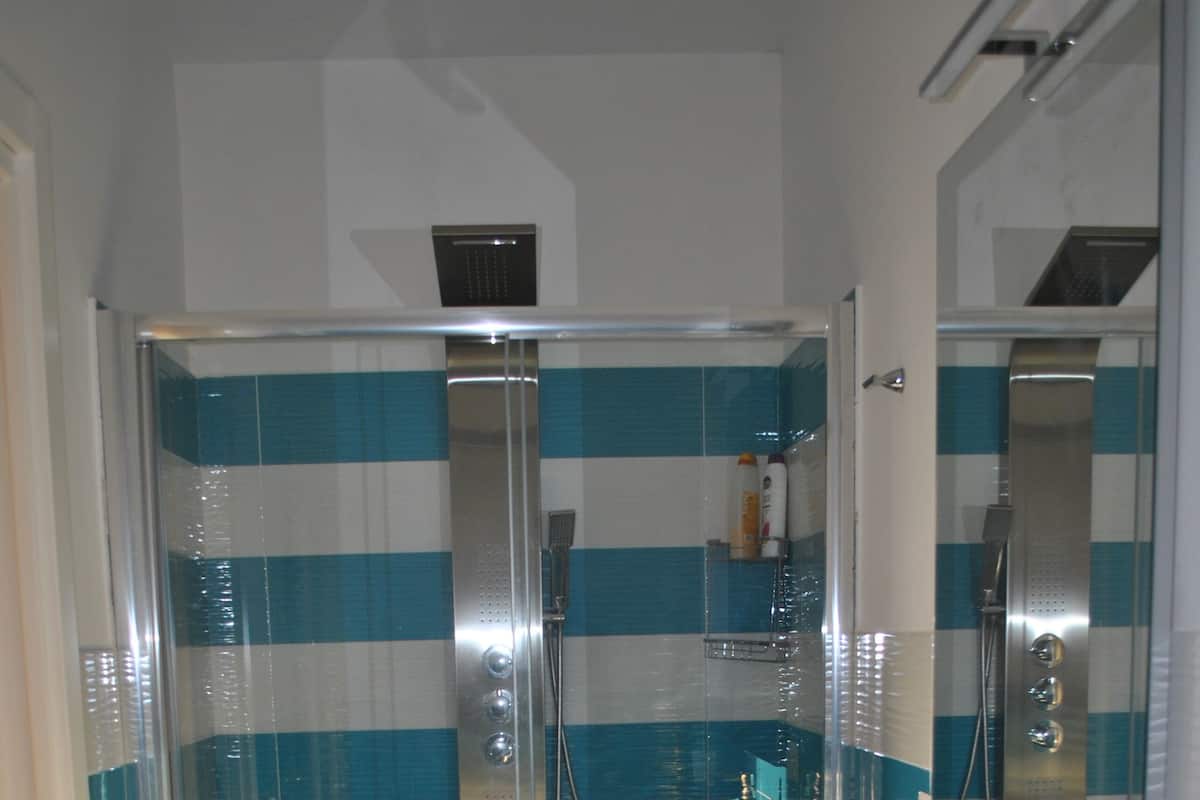 Une salle de bain avec une douche à parois de verre, un lavabo blanc avec un miroir et des carreaux bleus à rayures.