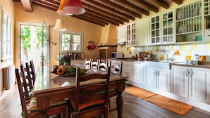 A kitchen with wooden beams, white cabinets, and a dining table with chairs. - Il Castagno (Camaiore)