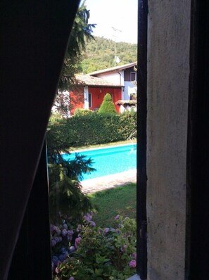 A view of a swimming pool surrounded by greenery and a building with a red facade. - Villa Cesarina (Vallio Terme)