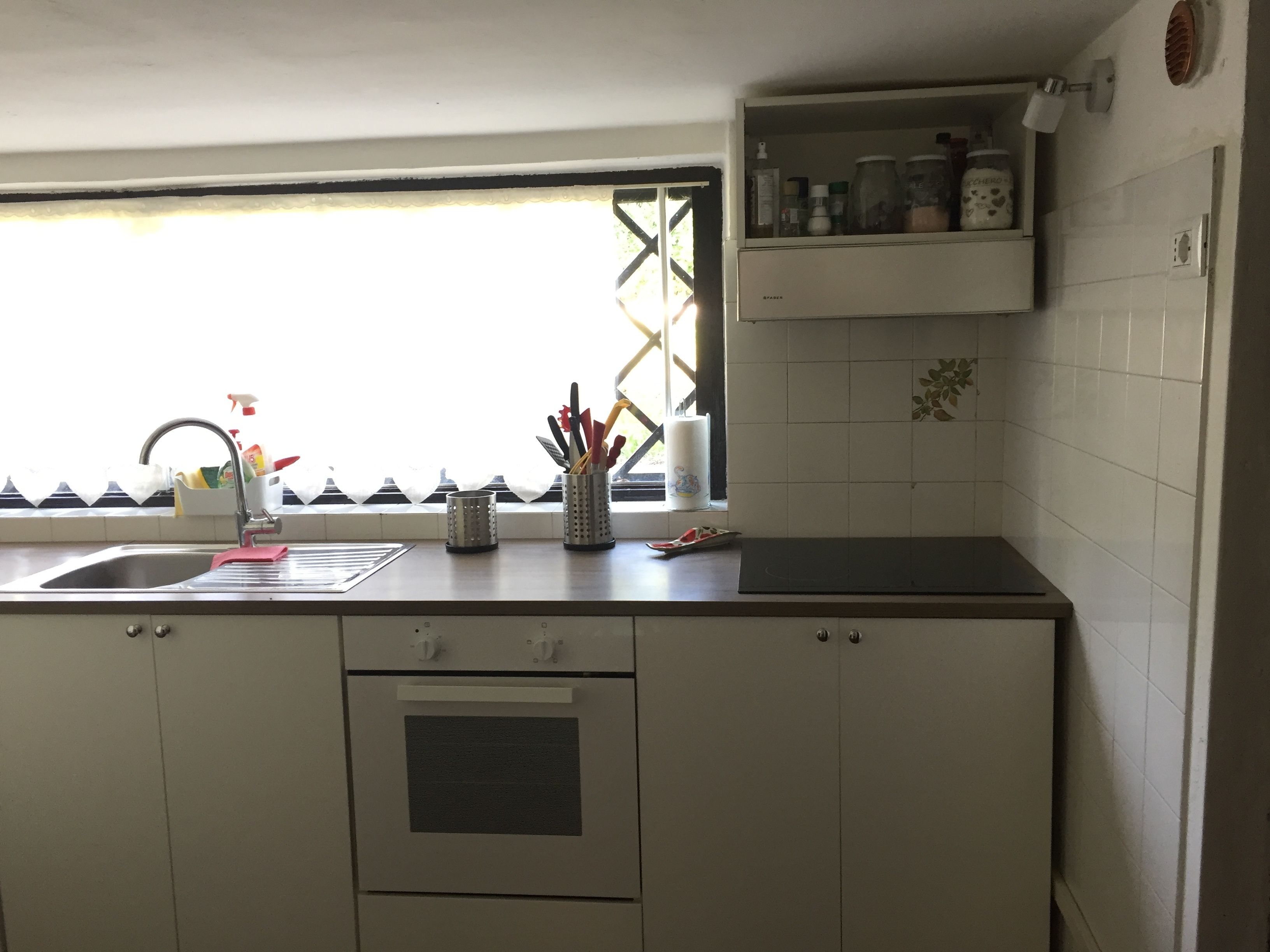 A kitchen with a sink, a window with a view, cabinets, and a countertop with various items.