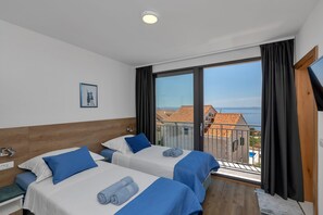 A hotel room with two beds, a large window with a view of buildings, a ceiling light, and a small picture on the wall. - Modern house with private pool, family-friendly, WiFi, barbecue, sea view, quiet (Makarska)