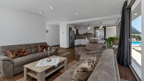 A modern living room with a sofa set, a coffee table, and a view of the kitchen and pool. - Modern house with private pool, family-friendly, WiFi, barbecue, sea view, quiet (Makarska)