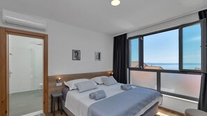 A bedroom with a large bed, a view of the sea, a window with curtains, and a small table. - Modern house with private pool, family-friendly, WiFi, barbecue, sea view, quiet (Makarska)