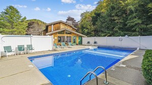 Una piscina rectangular amb una escala metàl·lica, envoltada per una tanca blanca, i un edifici de fusta amb una porta verda al fons.