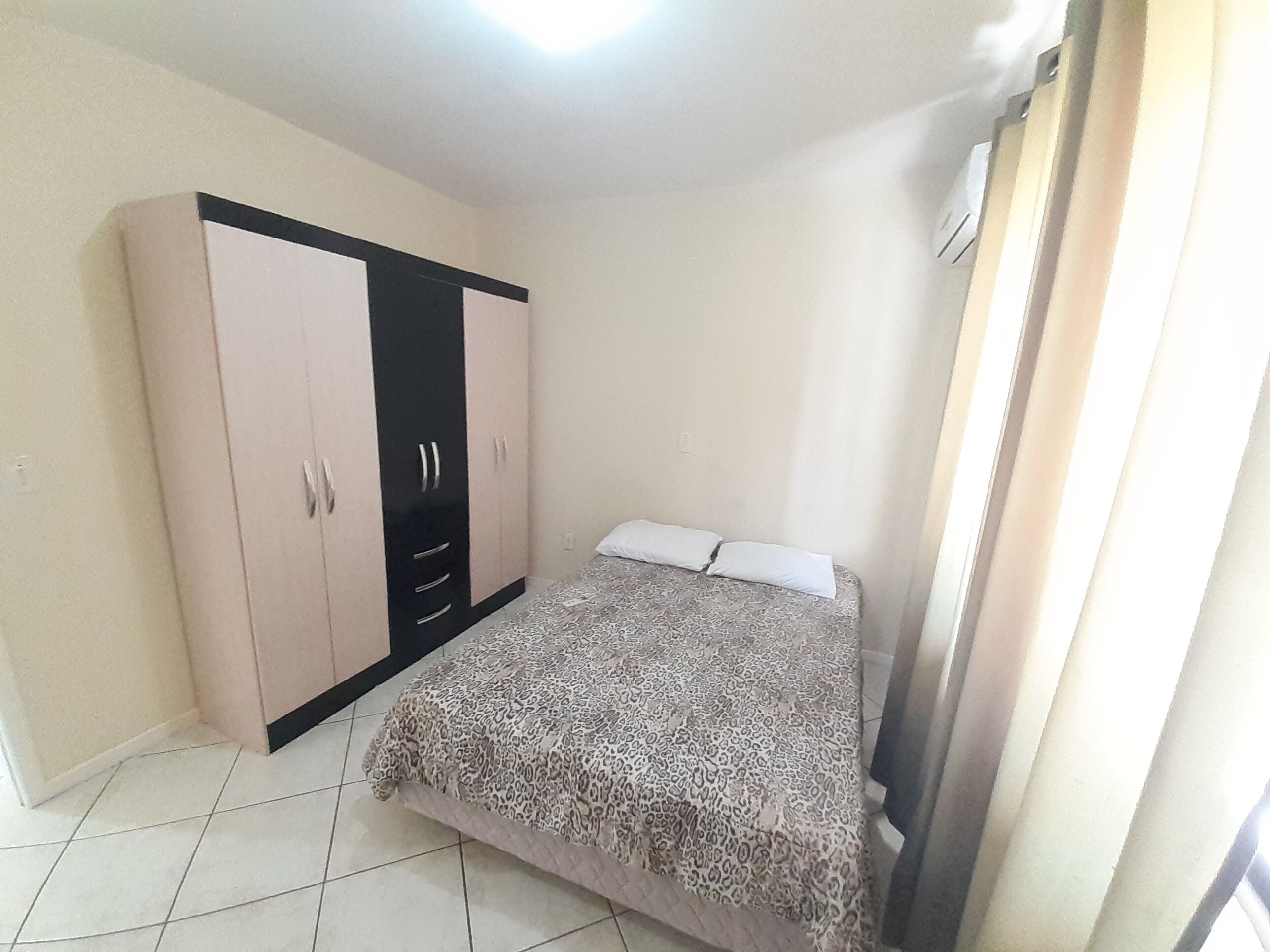 A bedroom with a bed, a wardrobe, and a window with curtains.