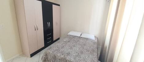 A bedroom with a bed, a wardrobe, and a window with curtains.