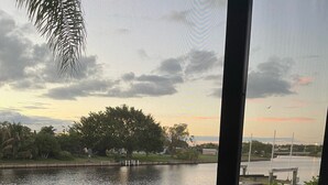 Vista de un río con un muelle y árboles, una mesa de vidrio con un martini, y una barandilla de balcón.