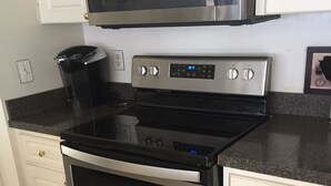 Una cocina con estufa de acero inoxidable, un microondas encima, armarios blancos y una cafetera en la encimera.