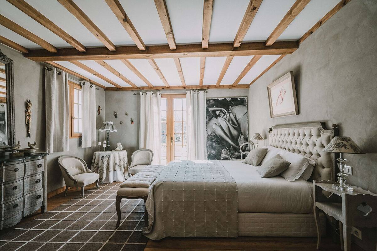 A bedroom with a large bed, a chair, a dresser, and a window.