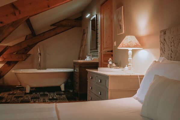Une chambre à coucher comprenant un lit, une table de chevet, une lampe, une commode, un miroir, une baignoire et une fenêtre.