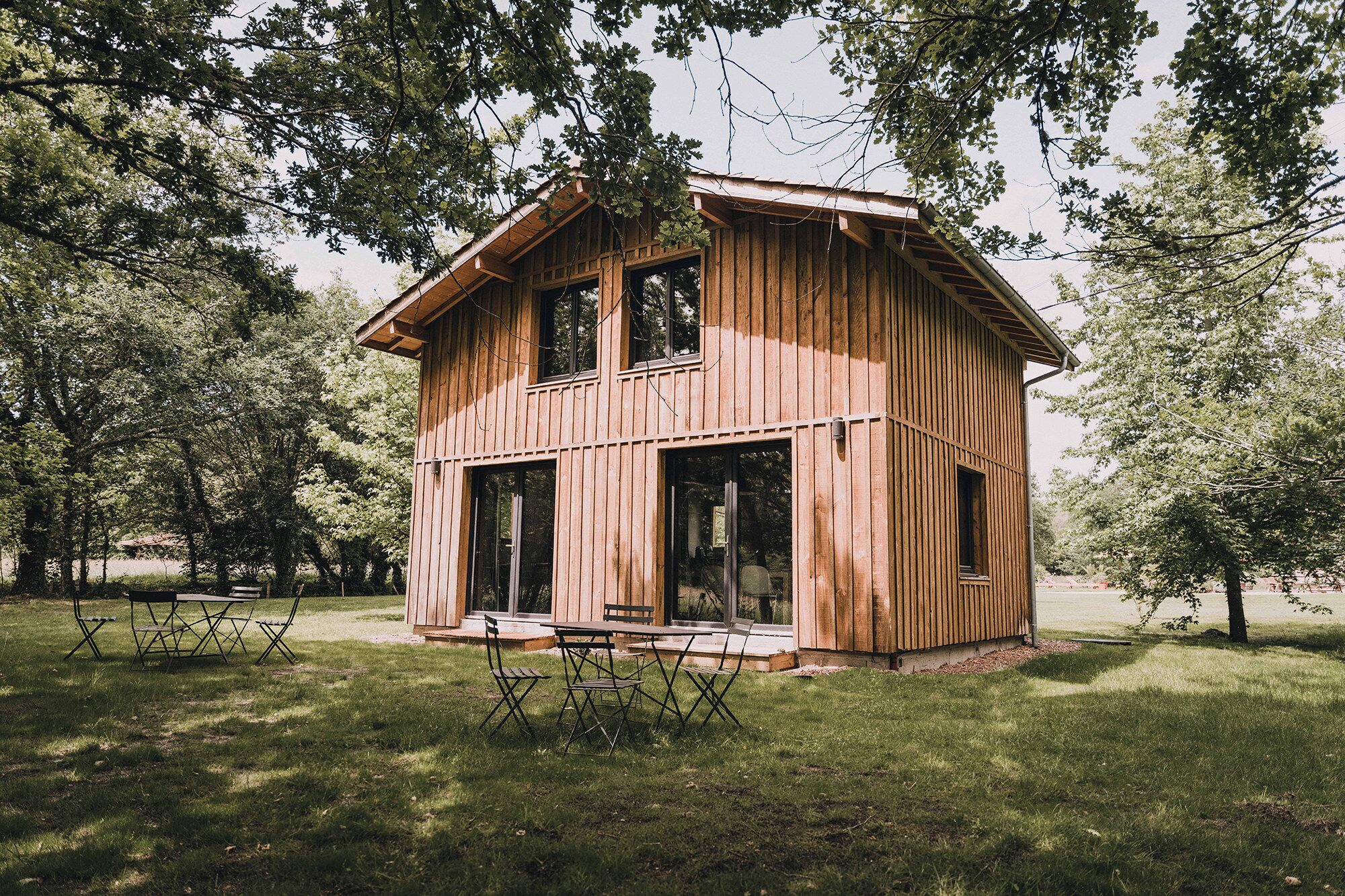 A wooden cabin with a porch and two windows, surrounded by trees.
