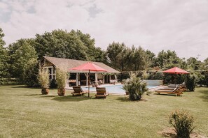 Une maison avec une piscine, entourée de pelouse et d’arbres.