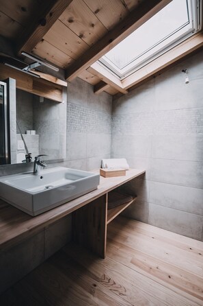 Une salle de bain moderne dotée d’un puits de lumière, d’un grand lavabo et d’un meuble-vasque en bois.