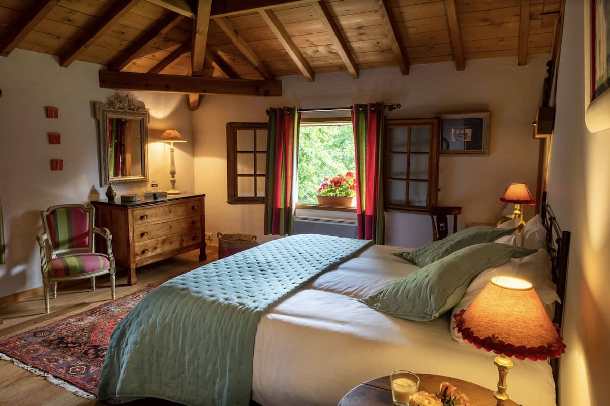 A bedroom with a bed, a dresser, a chair, and a window with curtains.
