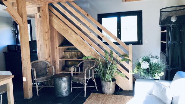 Una sala de estar acogedora con una escalera de madera, muebles de mimbre y un sofá blanco.
