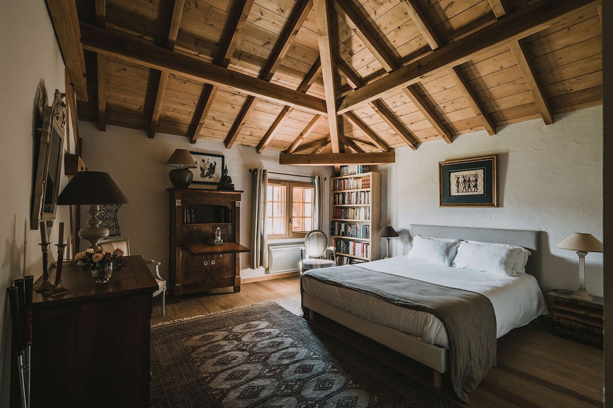 A bedroom with a wooden ceiling, a bed, a bookshelf, a desk, and a window.