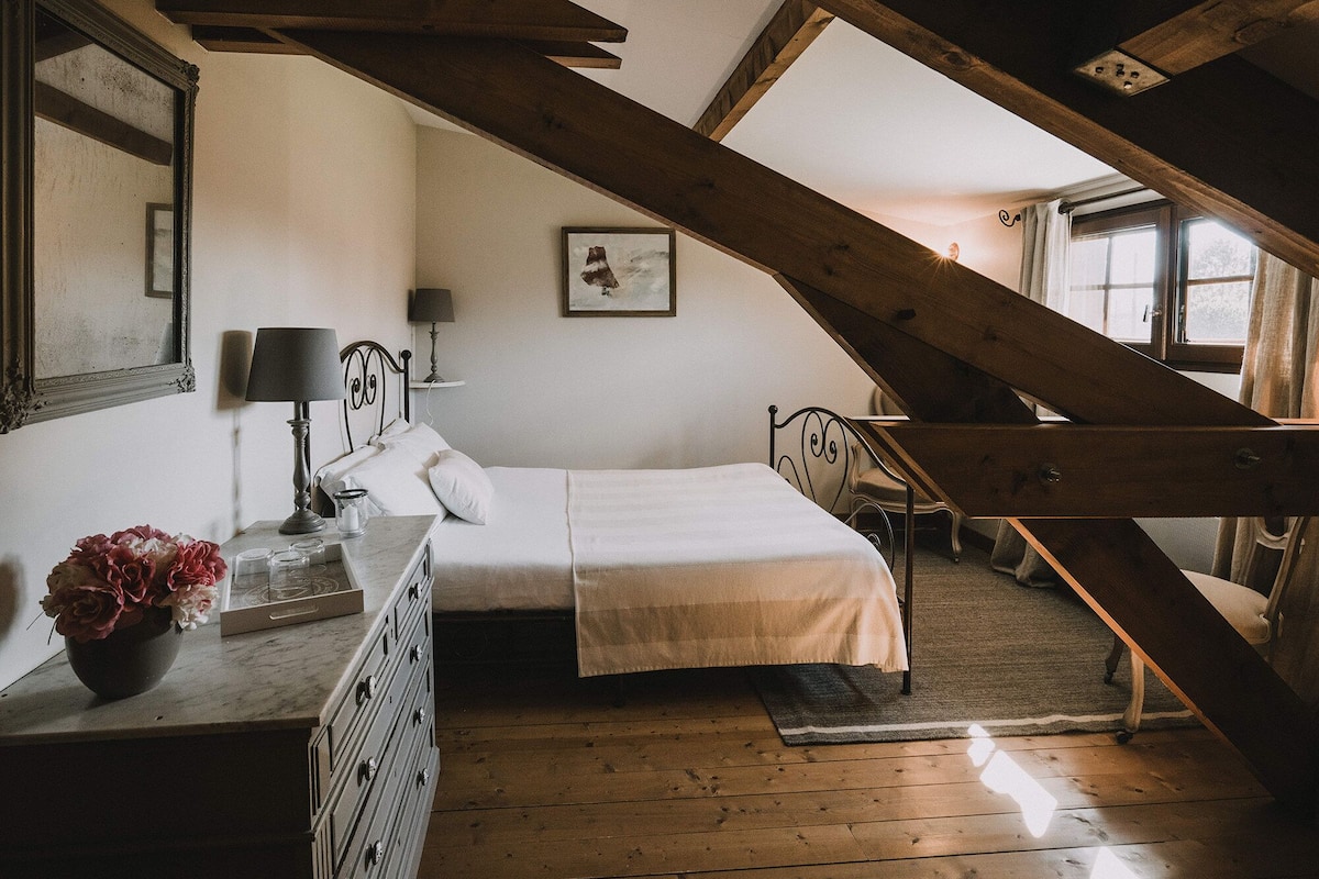 A bedroom with a wooden staircase, a bed, a dresser, a mirror, and a framed picture on the wall.