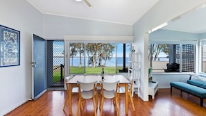 A modern living space with a dining area, a sofa, and large windows offering a view of the sea.