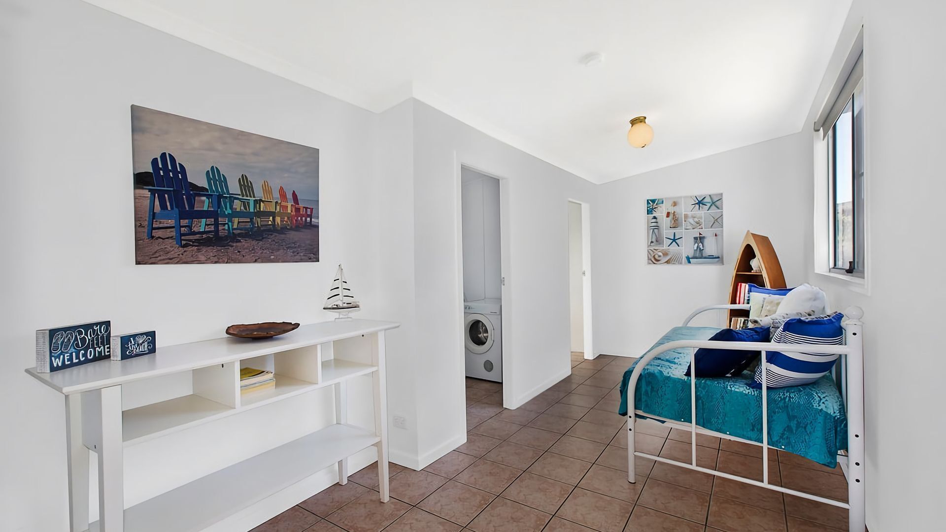 A bedroom with a bed, a white console table, a painting, and a window.