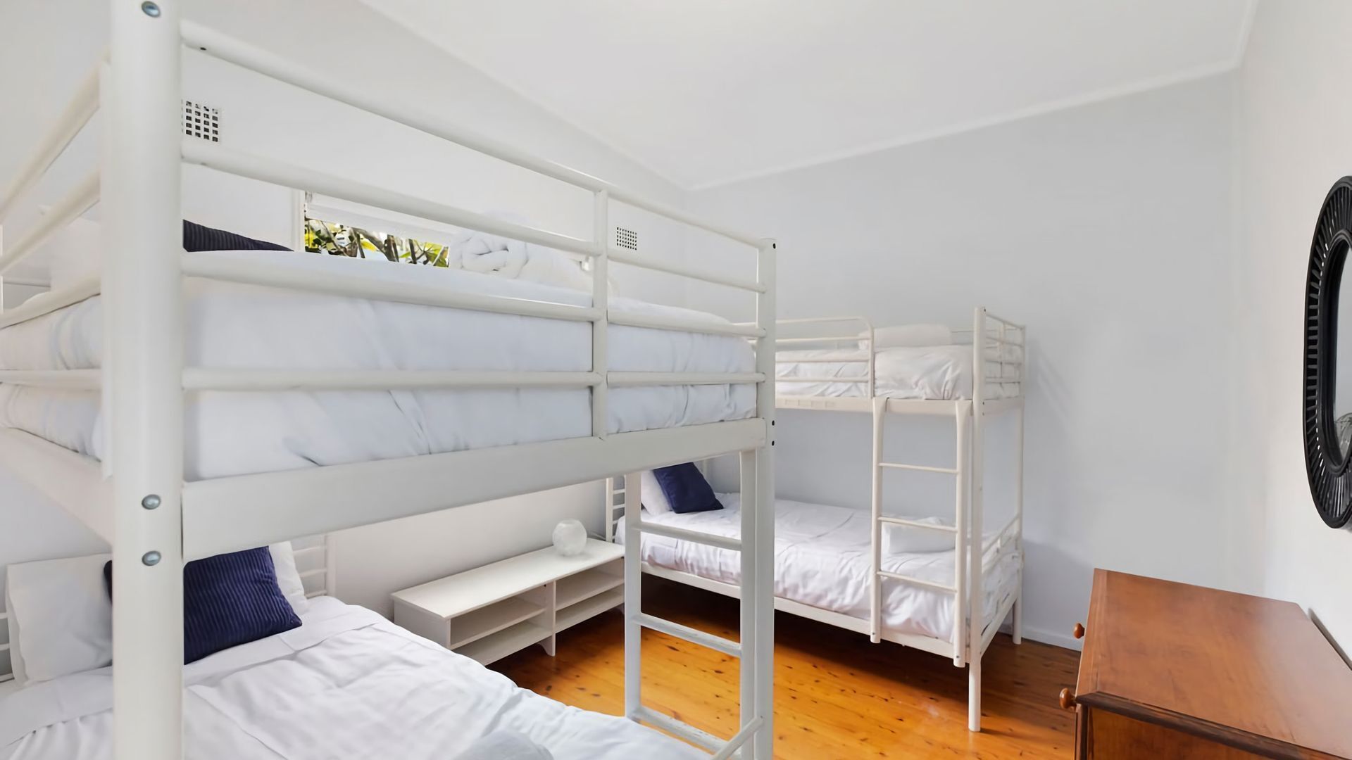 Une chambre avec un lit superposé, un plancher en bois, des murs blancs et une petite table en bois.