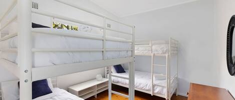 Une chambre avec un lit superposé, un plancher en bois, des murs blancs et une petite table en bois.
