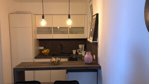 Een moderne keuken met witte kastjes, een donker aanrecht en twee hanglampen.