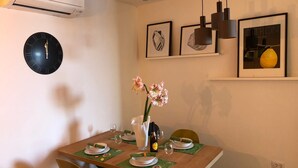 Een eetruimte met een houten tafel gedekt voor vier personen, een wandklok en ingelijste kunstwerken erboven.