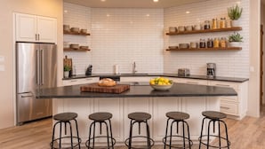 Une cuisine moderne avec des carreaux de céramique blancs disposés en motif métro, des appareils en acier inoxydable, des tabourets de bar en bois et des étagères intégrées.